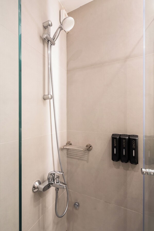 A shower with a handheld showerhead and a wall-mounted faucet. There are three black bottles labeled "HAIR," "BODY," and "COND" on the wall.