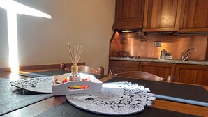 Een eettafel met een middelpunt, houten kasten en een keukenhoek.