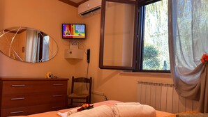 Een hotelkamer met een bed, een televisie, een spiegel, een raam met gordijnen en een radiator.