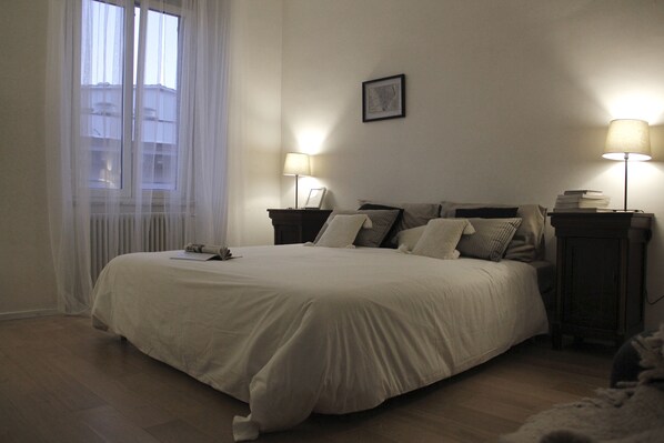A neatly made bed in a hotel room with a large window, two bedside tables with lamps, and a framed picture on the wall. - Urbanflat - Central Rome (Roma)