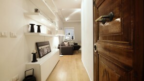 A hallway with a wooden door, a white wall with shelves, a framed picture, and a floor lamp. - Urbanflat - Central Rome (Roma)