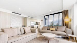 A modern living room with two sofas, a coffee table, and a view of the city through large windows. - Breeze Apartment 801 (Mooloolaba)