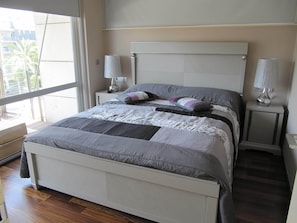 Cozy retreat with a large bed, white headboard, and bedside tables, set against a neutral backdrop.