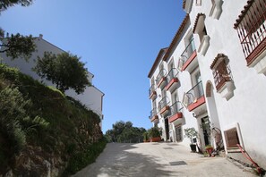 Uma rua estreita com edifícios em ambos os lados, com varandas e guarda-corpos com plantas em vasos.