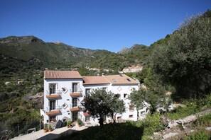 Um edifício de dois andares com telhado de azulejos, rodeado por vegetação e montanhas.