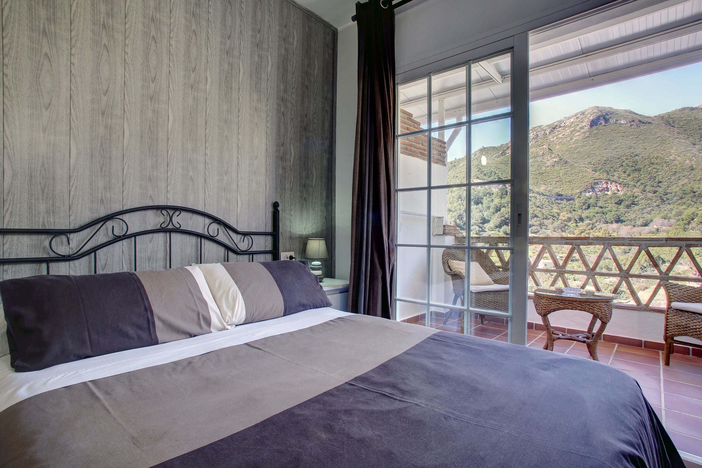 Ein Schlafzimmer mit einem großen Bett, Bergblick vom Balkon und einem Korbstuhl.
