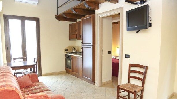 Een compacte leefruimte met een kitchenette, een bank, een eettafel en een televisie.