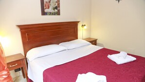 Een netjes opgemaakt bed met witte lakens, een houten hoofdbord en een rode sprei. Er zijn twee nachtkastjes met lampen en een wanddecoratie boven het bed.