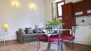 Un coin repas avec une table et des chaises, un canapé, une lampe et, au fond, une cuisine.