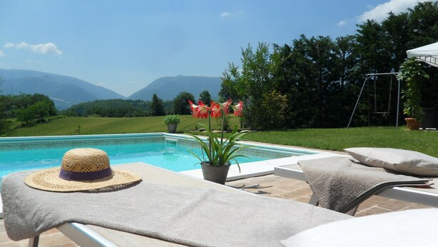 Un área junto a la piscina con sillones de descanso, un sombrero y una planta en maceta.