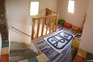 A staircase with a wooden handrail leading to a landing. A colorful rug with a road design is on the landing.