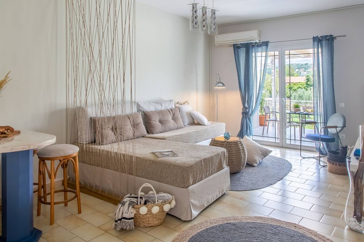 Una sala de estar moderna con un sofá, una mesa de comedor y una mesita auxiliar. Se ve el exterior a través de una puerta de vidrio.