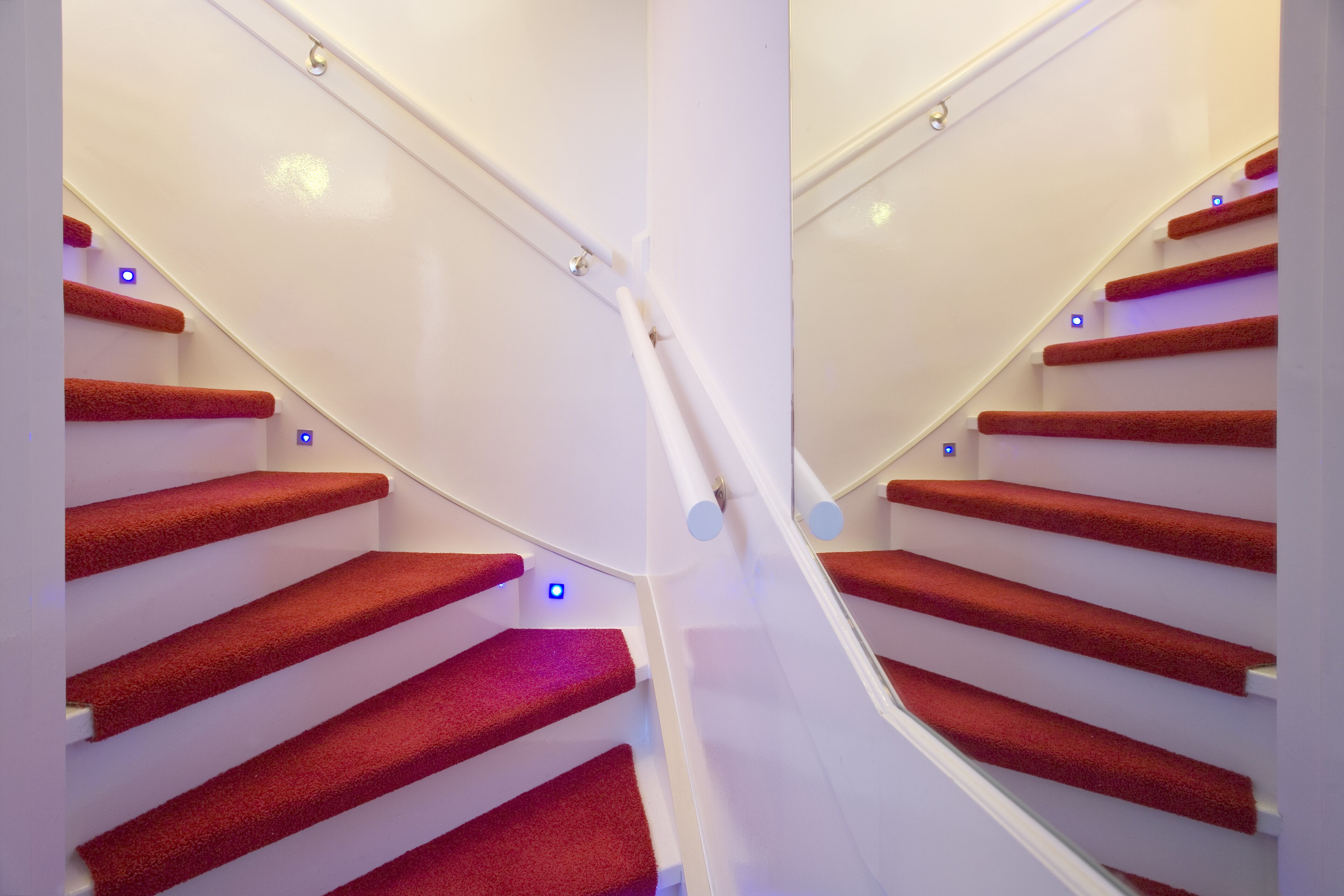 A staircase with red carpeted steps and white walls, featuring a modern design with a glass railing and blue LED lights.