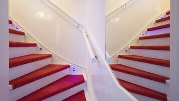 A staircase with red carpeted steps and white walls, featuring a modern design with a glass railing and blue LED lights.