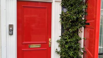 A red door with a brass handle and a mail slot, a window above it, and a house number '18' on the wall.