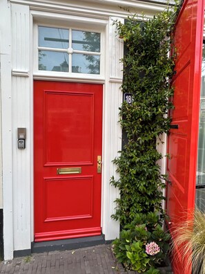A red door with a brass handle and a mail slot, a window above it, and a house number '18' on the wall. - MAFF TOP APARTMENT | city ​​center - private parking (Den Haag)