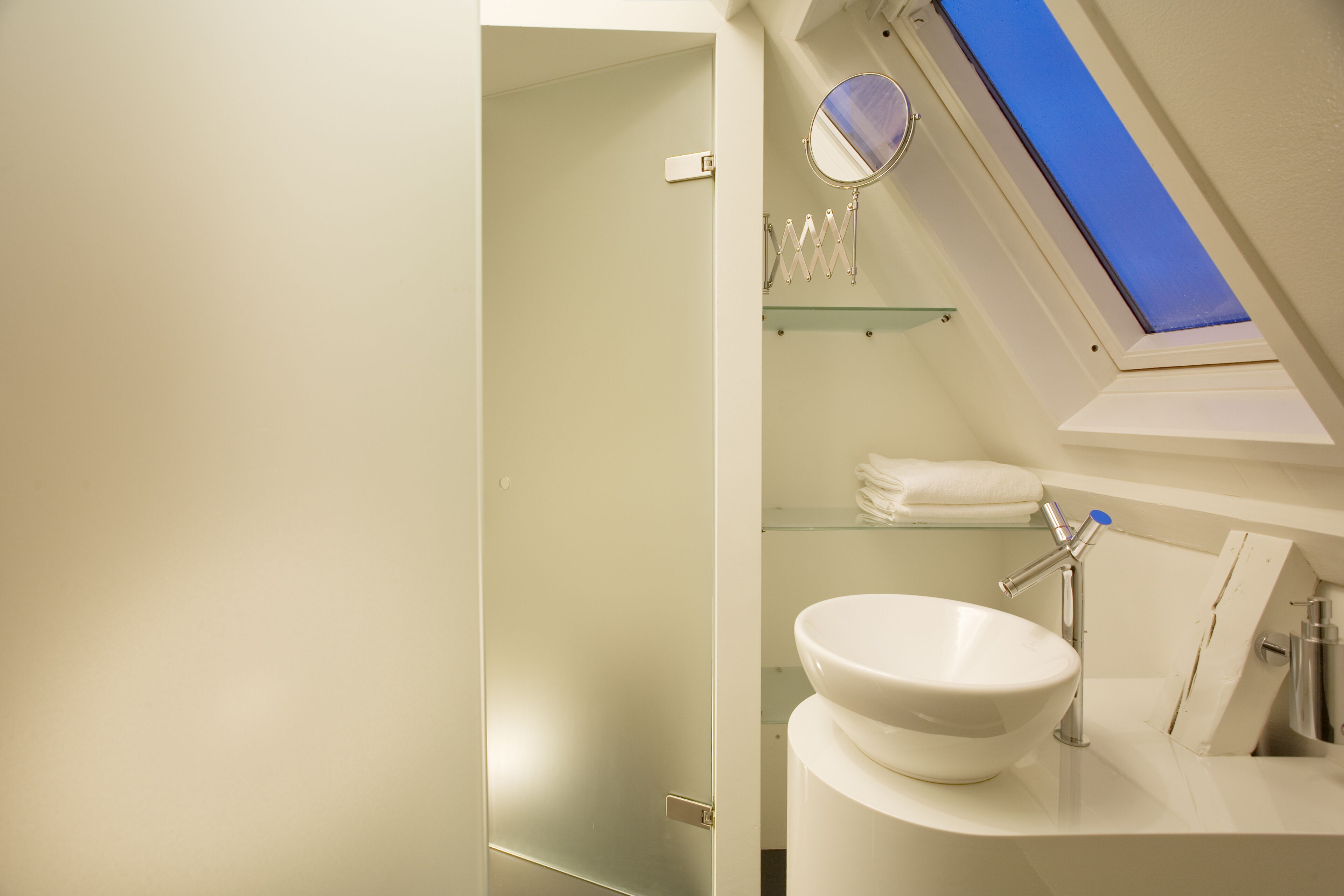 A modern bathroom with a skylight, a large white sink, and a glass shelf.
