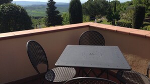 A balcony with a table and chairs, overlooking a scenic landscape with trees and hills. - Apartment for 6 with 3 rooms near San Gimignano and Volterra. (montaione)
