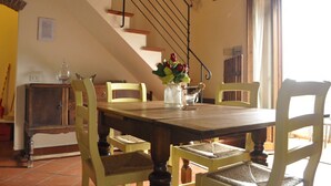 A dining area with a wooden table, four chairs, a vase with flowers, a staircase, and a cabinet. - Apartment for 6 with 3 rooms near San Gimignano and Volterra. (montaione)