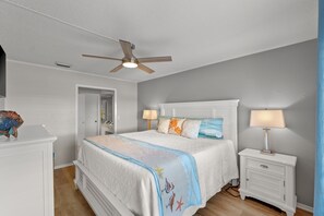 A bedroom with a bed, nightstands, a ceiling fan, and a door. - Cajun Fun 1060 - 1 Br Condo (Destin)