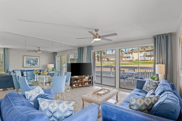 A spacious living room with a large TV, comfortable seating, and a balcony with a view. - Cajun Fun 1060 - 1 Br Condo (Destin)