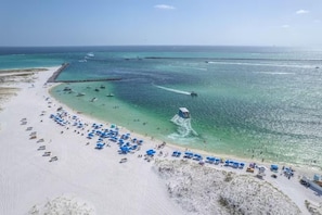 En strand med kristallklart turkost vatten, en sandstrand och ett stort antal blåa parasoller.