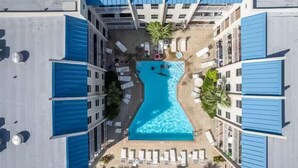 A rooftop pool surrounded by blue awnings and white walls, with lounge chairs and a palm tree.