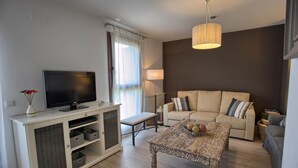 Ett modernt vardagsrum med en platt-TV, en soffa, ett soffbord och en lampa.