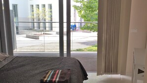 A bedroom with a large bed, a sliding glass door leading to an outdoor area, and a view of a building and street.