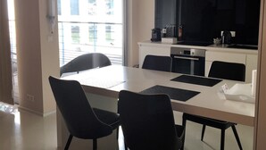 A modern kitchen with a flat-screen TV, a dining table with chairs, and a large window providing natural light.