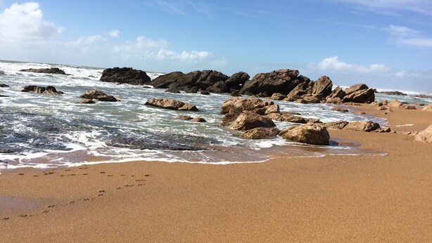 Une plage de sable avec de gros rochers et des vagues.