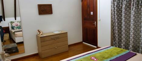 A bedroom with a bed, a wooden dresser, a wardrobe, a mirror, and a patterned curtain.