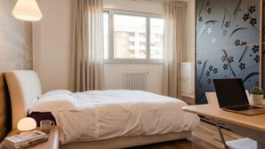A hotel room with a bed, a desk with a laptop, a window with curtains, and a radiator. - Appartamento Gassman - Holiday Apartment in Milano (Milano)