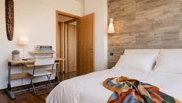 A bedroom with a bed, a desk with a chair, a lamp, and a wooden wall panel.