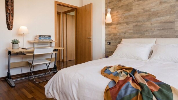 A bedroom with a bed, a desk with a chair, a lamp, and a wooden wall panel. - Appartamento Gassman - Holiday Apartment in Milano (Milano)