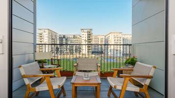 A balcony with wicker chairs and a table, overlooking a residential area with buildings.