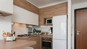 A modern kitchen with wooden cabinetry, a white refrigerator, an oven, and a microwave. - Appartamento Gassman - Holiday Apartment in Milano (Milano)