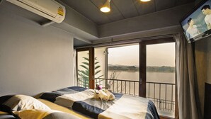 A hotel room with a bed, a TV, and a large window with a view of the water. - Chic Chiangkhan Hotel (Chiang Khan)