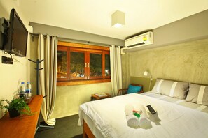 A hotel room with a bed, a TV, a desk with a plant, a window with curtains, and an air conditioning unit. - Chic Chiangkhan Hotel (Chiang Khan)
