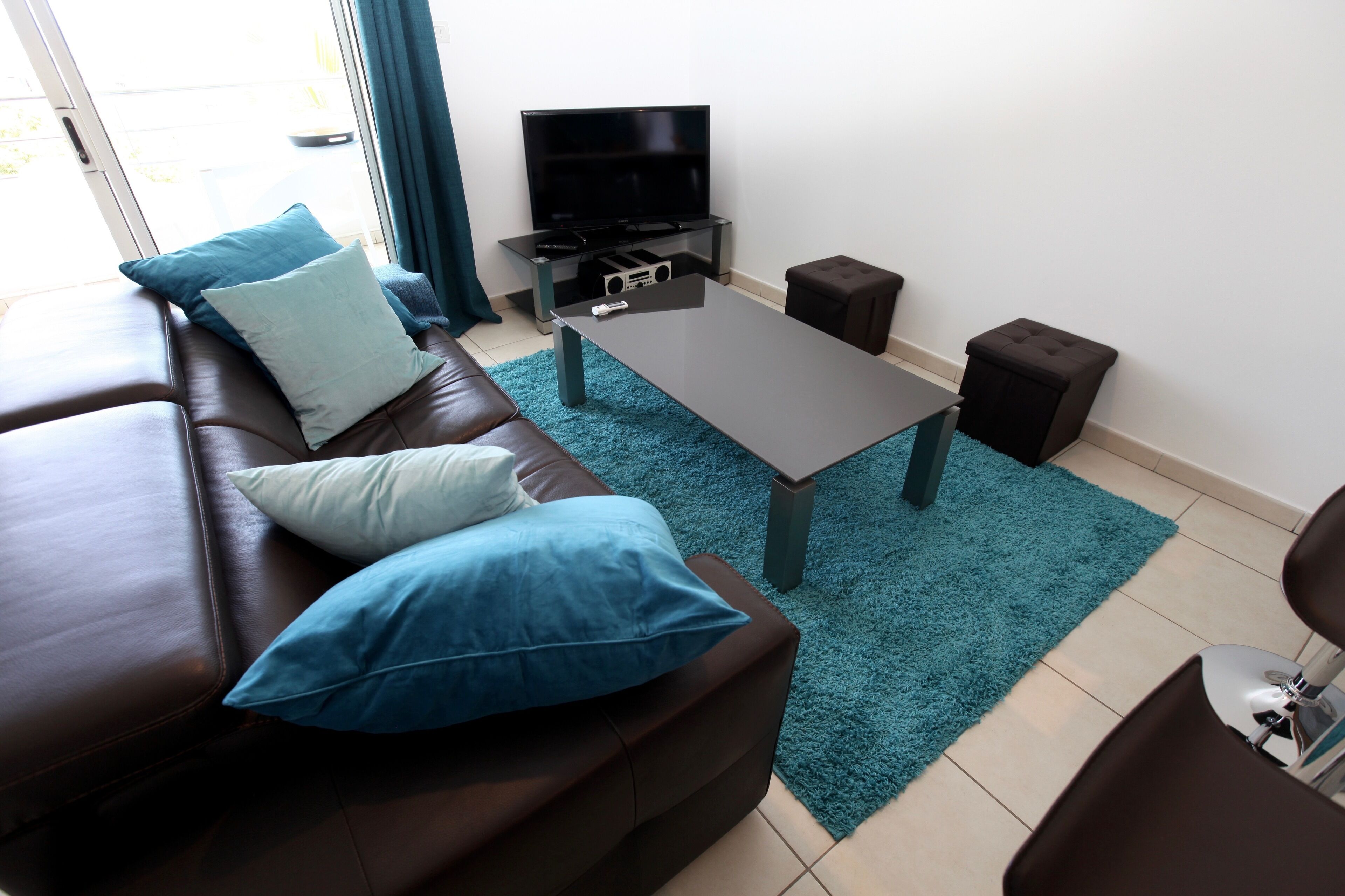 A modern living room with a leather sofa, a coffee table, a flat-screen TV, and a small ottoman.