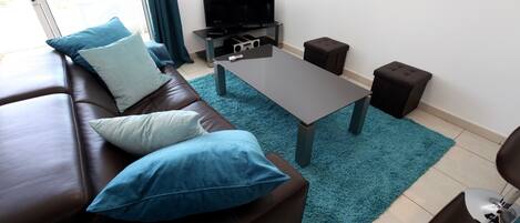 A modern living room with a leather sofa, a coffee table, a flat-screen TV, and a small ottoman.