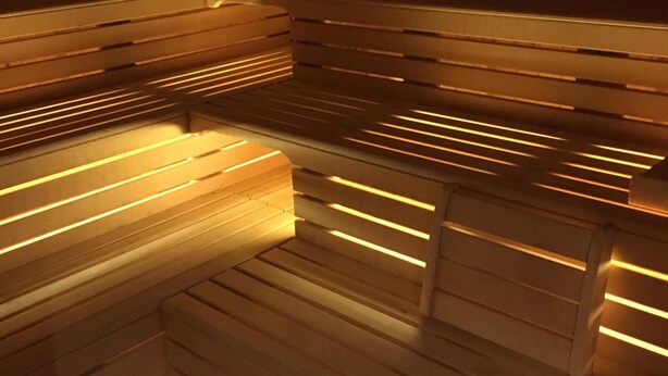 Un sauna avec des bancs en bois et des murs à lattes, éclairé par un éclairage chaleureux.