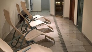 Un couloir bordé de rangées de chaises, une horloge au mur et une grille d’aération.