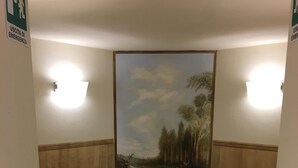 Un couloir orné d’une fresque représentant une scène de forêt, avec deux appliques murales et un sol carrelé.