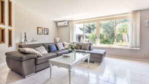Uma sala de estar com um sofá modular, uma mesa de centro de vidro e uma janela grande com cortinas.