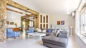Uma sala de estar ampla, com um arco de pedra, um sofá cinzento, poltronas azuis e uma mesa de centro branca.