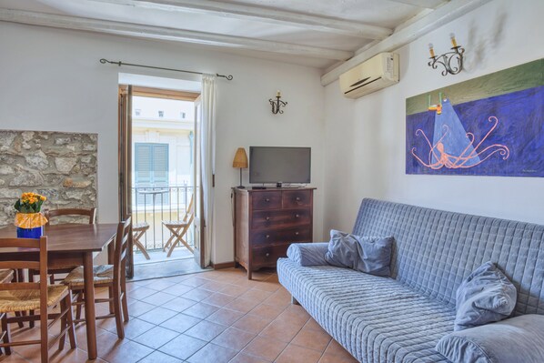 Een woonkamer met een bank, een televisie, een houten tafel met stoelen, een stenen muur en een balkon met uitzicht.