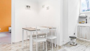 A white dining table with four chairs, a black pendant light, and a window with white curtains.