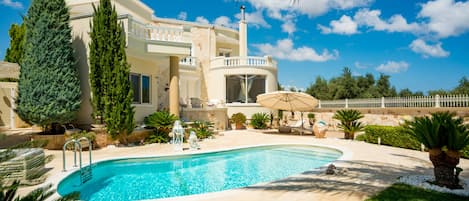 A large house with a swimming pool, surrounded by palm trees and a well-maintained lawn.