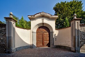Un mur de pierre avec une porte en bois et un chemin pavé de briques menant à cette porte.